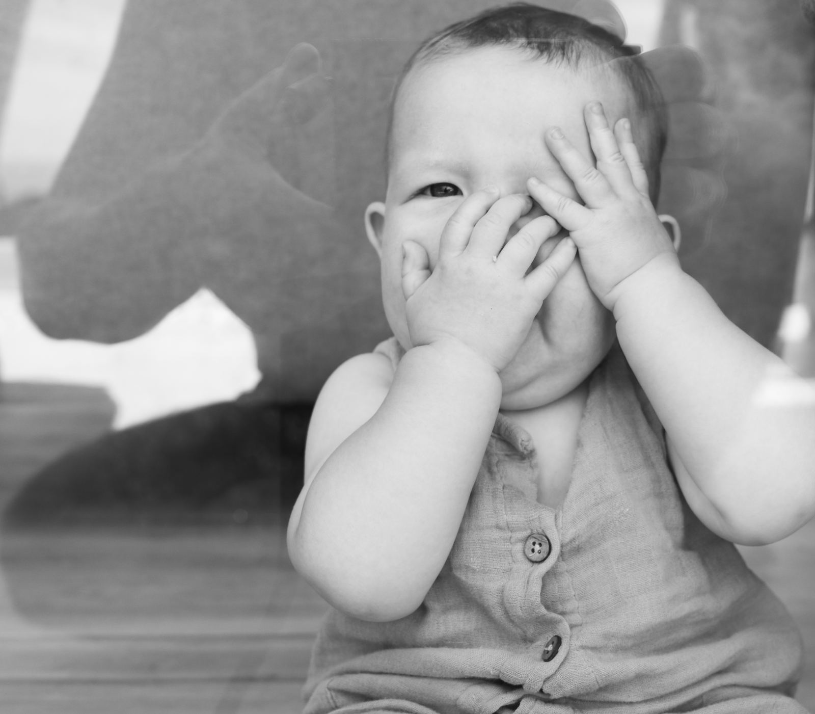 Baby hält sich lachend die Hände vors Gesicht